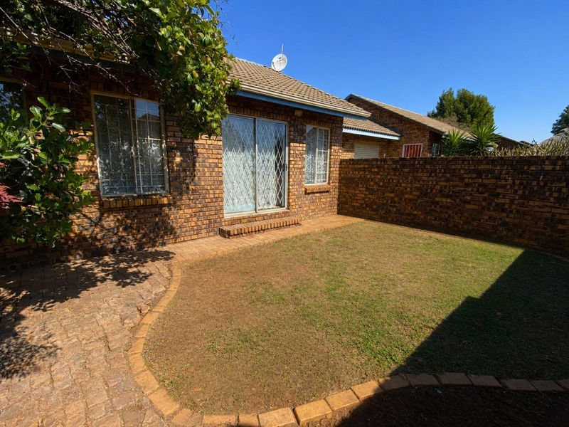 A private rear garden featuring a paved patio area, face-brick exterior, and secure sliding door access to the townhouse interior.