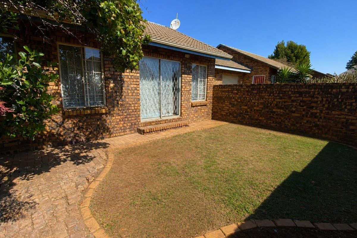 A private rear garden featuring a paved patio area, face-brick exterior, and secure sliding door access to the townhouse interior.