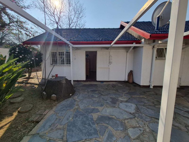 Rear exterior view of the cottage featuring a stone-paved patio area, metal pergola structure, and secure access points.
