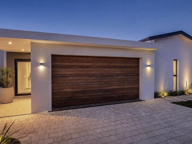 Modern front facade featuring a timber garage door, paved driveway, and integrated exterior lighting, showcasing a clean and contemporary architectural design.