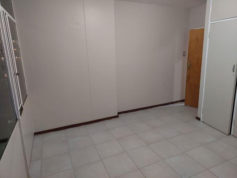 An empty bedroom featuring tiled flooring, built-in cupboard storage, and a wooden door, offering a blank canvas for potential renovation or styling.