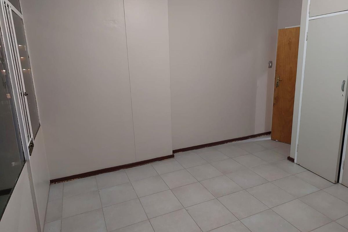 An empty bedroom featuring tiled flooring, built-in cupboard storage, and a wooden door, offering a blank canvas for potential renovation or styling.