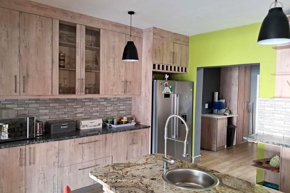 Modern kitchen featuring wood-look cabinetry, granite countertops, a central island with a prep sink, and a subway tile backsplash.