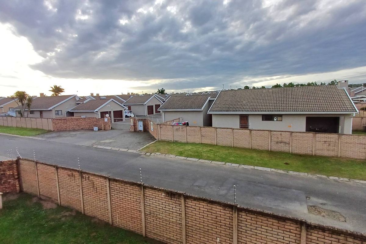 Elevated view of a residential complex featuring multiple single-story units with tiled roofs, enclosed by perimeter brick walls with security fencing.