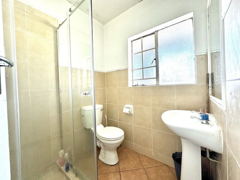 A functional bathroom featuring a pedestal basin, toilet, and a glass-enclosed shower with neutral wall and floor tiling.