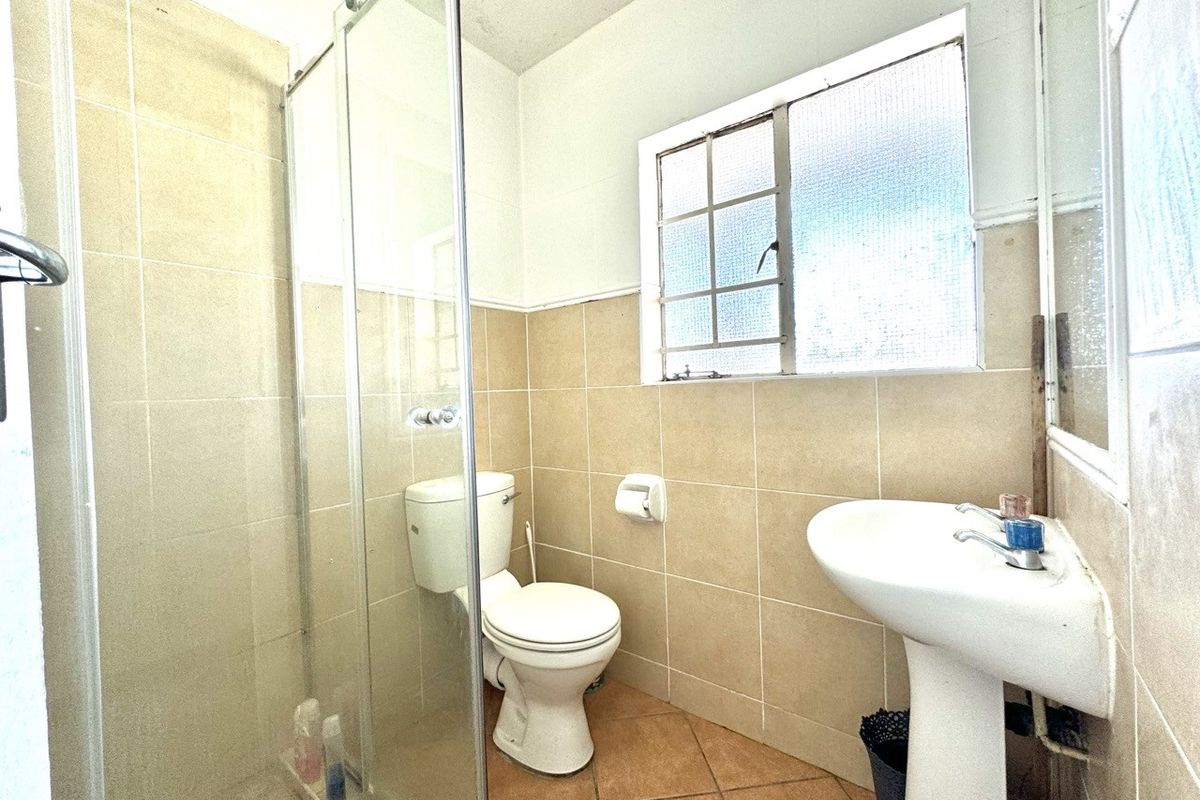 A functional bathroom featuring a pedestal basin, toilet, and a glass-enclosed shower with neutral wall and floor tiling.