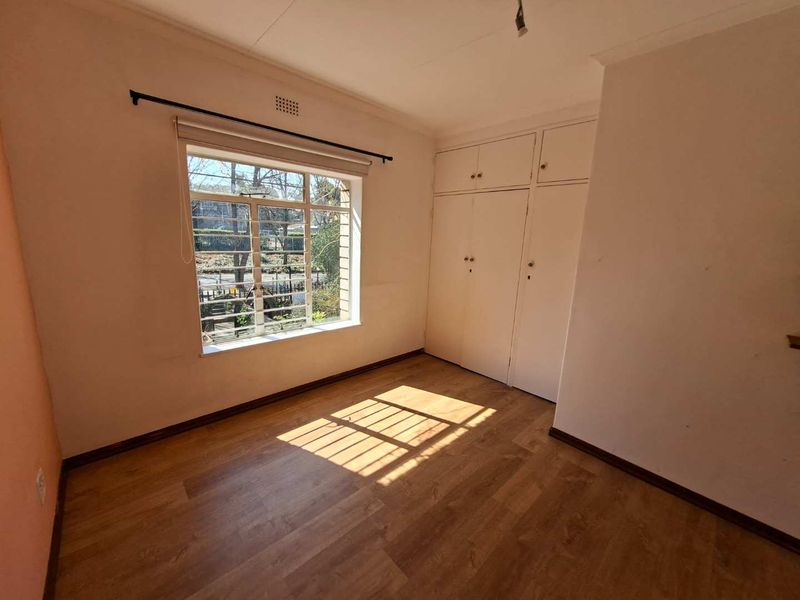 A vacant bedroom featuring laminate flooring, built-in cupboards, and a large steel-framed window allowing natural light.