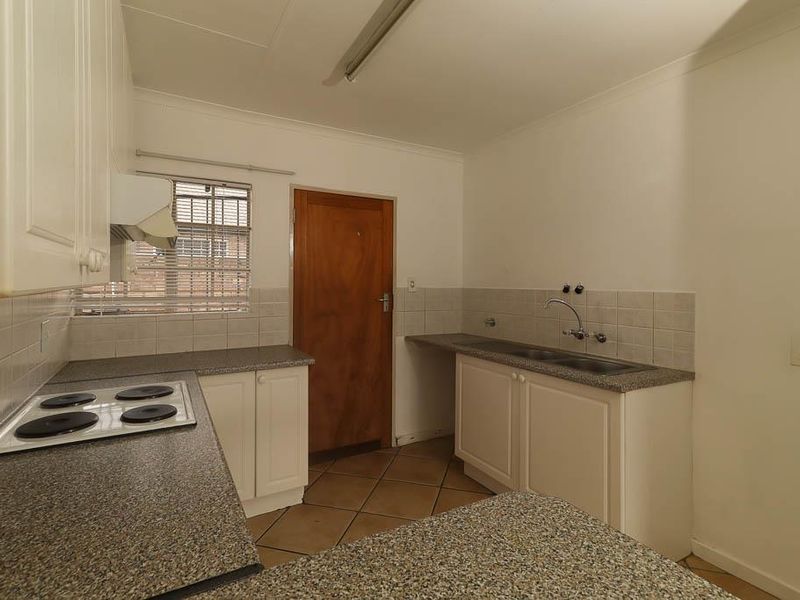 A functional kitchen featuring built-in cabinetry, laminate countertops, a double stainless steel sink, and an integrated electric hob with an extractor fan.