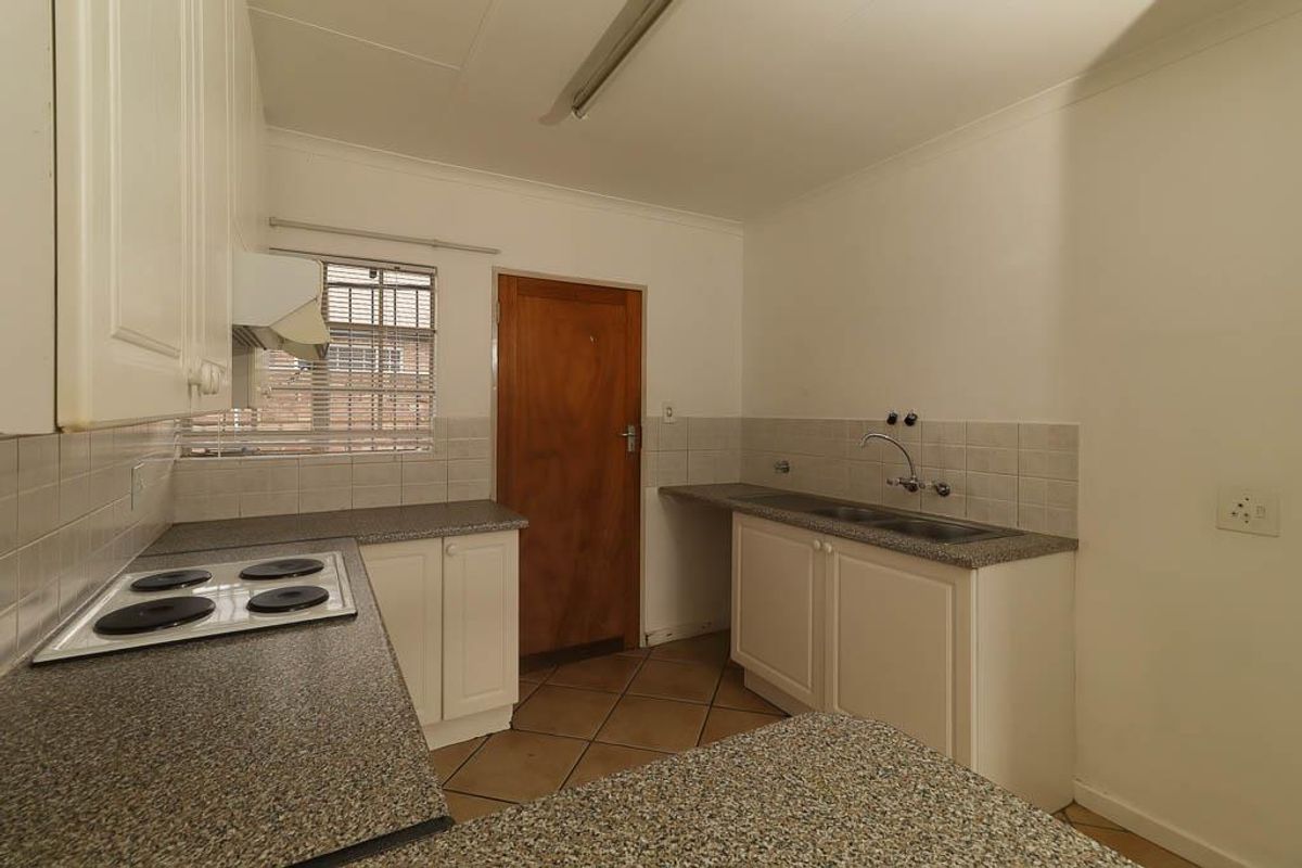 A functional kitchen featuring built-in cabinetry, laminate countertops, a double stainless steel sink, and an integrated electric hob with an extractor fan.