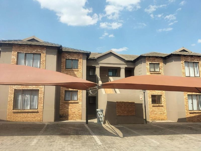 Front elevation of a multi-story apartment complex featuring brick accents, tiled roofing, and dedicated paved parking bays with shade cloth carports.