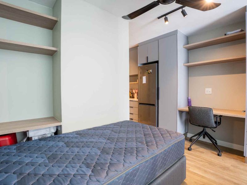 A modern bedroom featuring built-in desk space, integrated shelving, cabinetry, and laminate flooring, with a ceiling fan and track lighting.