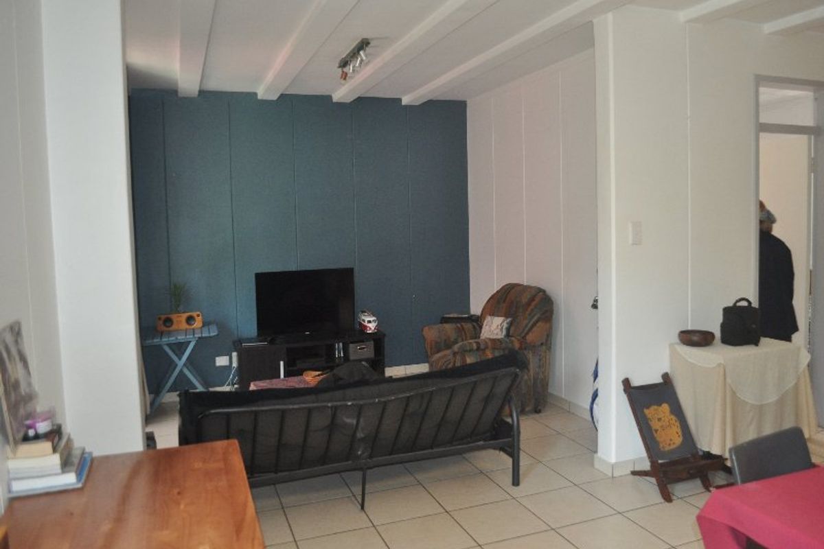 A living room area featuring tiled flooring, an accent wall, and exposed ceiling beams, providing a functional space for relaxation.