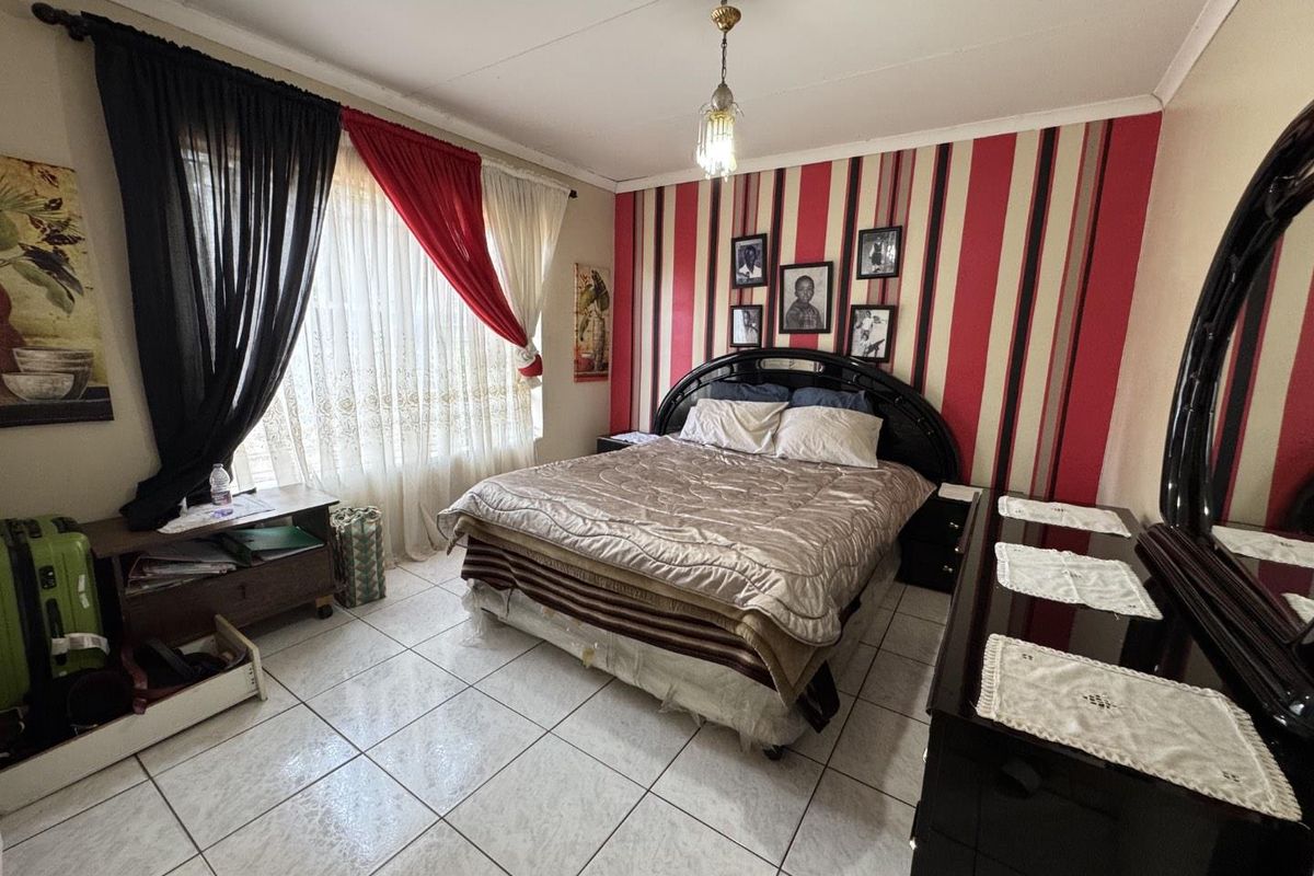 A bedroom featuring tiled flooring, a feature wall with vertical striped wallpaper, and a central pendant light fixture.