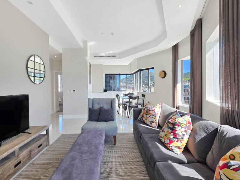 Spacious open-plan living and dining area featuring modern tiled floors, recessed lighting, ducted air conditioning, and large windows with city and mountain views.