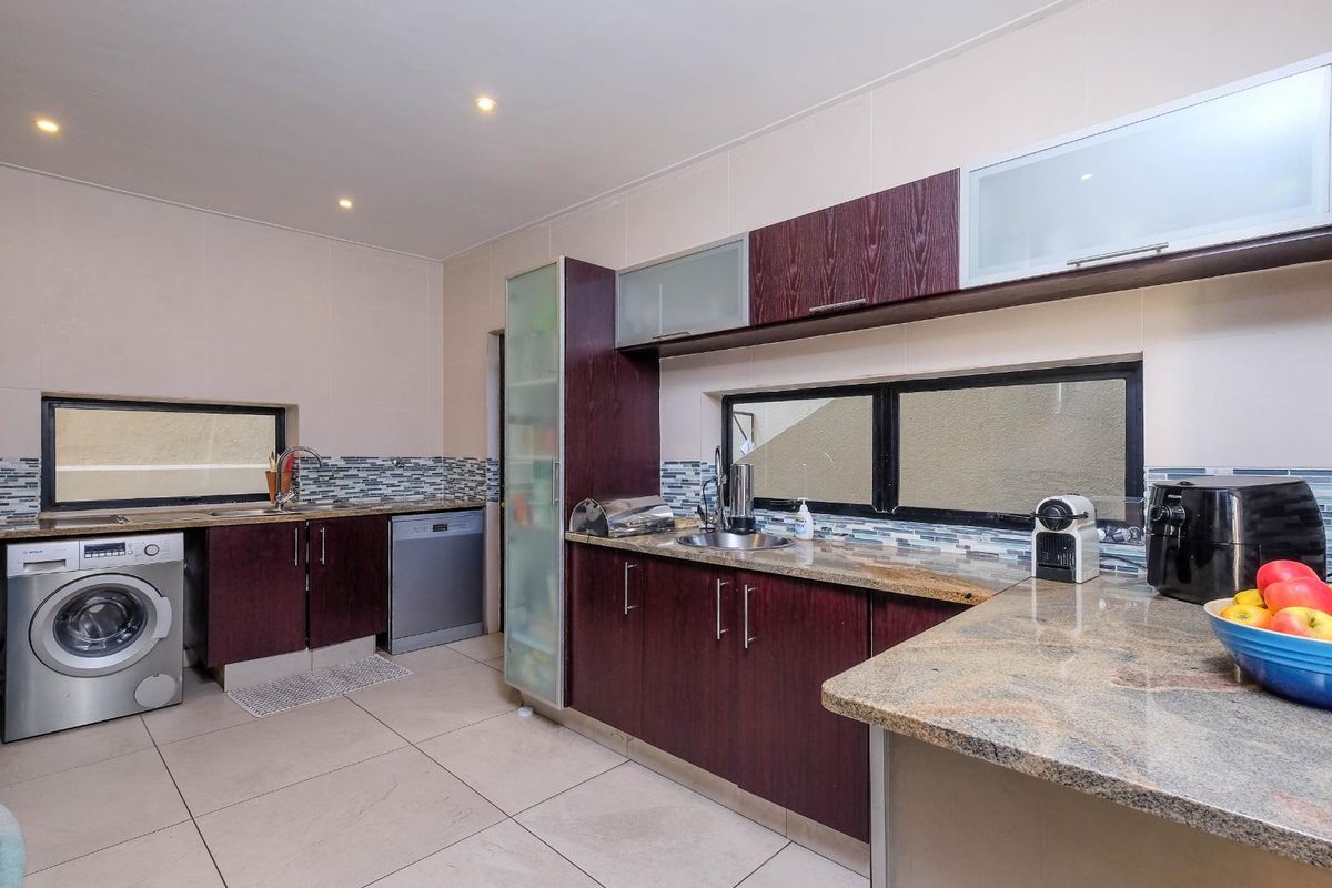 A functional kitchen featuring dark wood cabinetry, granite countertops, mosaic tile backsplash, and integrated space for laundry appliances.