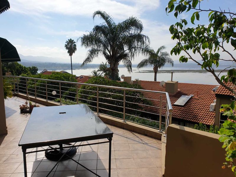 Spacious elevated balcony featuring tiled flooring and stainless steel railings, offering expansive views over the surrounding landscape and water.