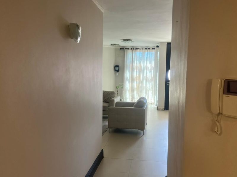 A view from a hallway looking into a living area, featuring tiled flooring, a wall-mounted intercom, and neutral wall finishes.