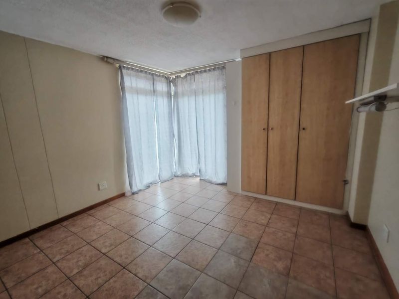 An empty bedroom featuring tiled flooring, built-in wooden cupboards, and natural light through corner windows.