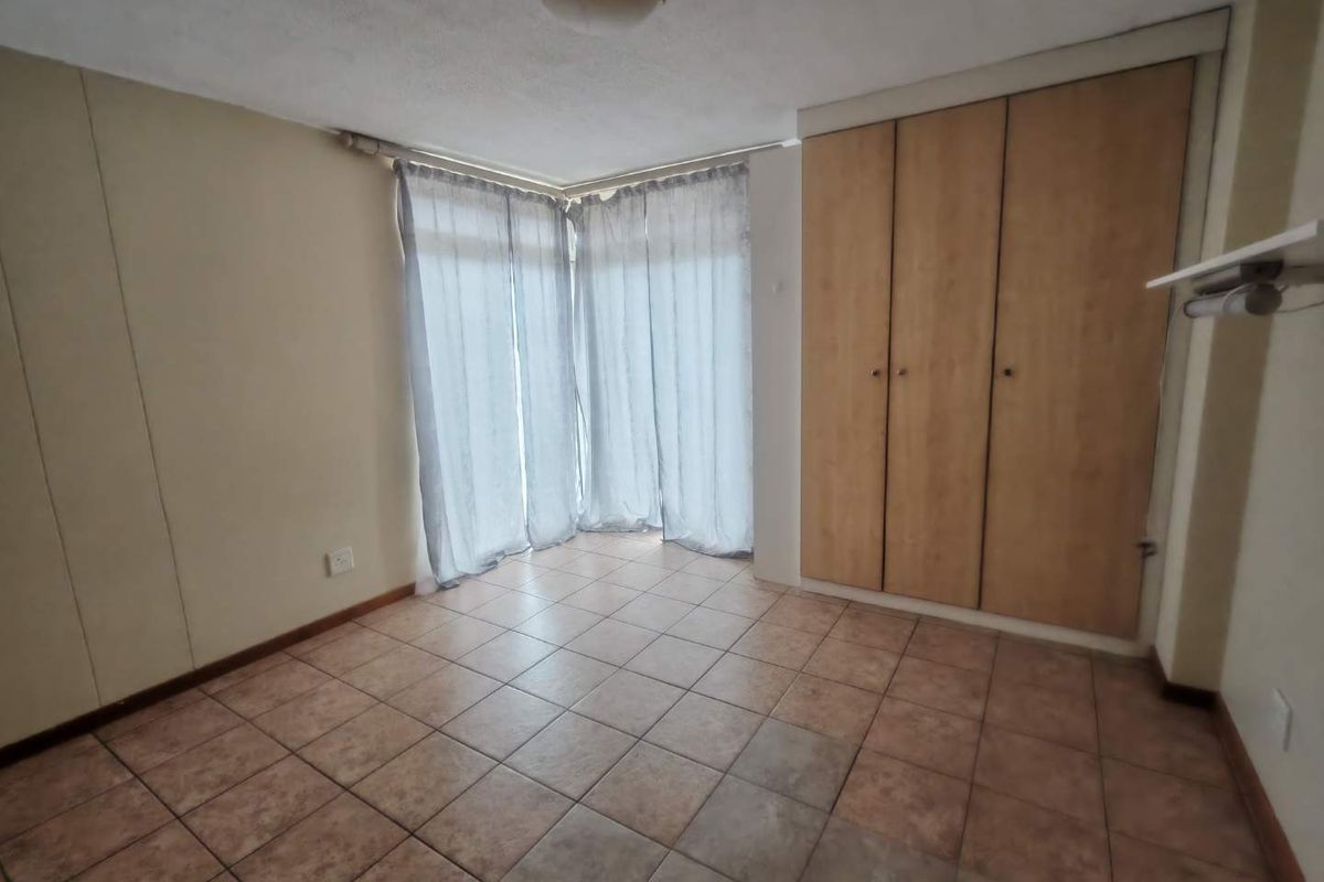 An empty bedroom featuring tiled flooring, built-in wooden cupboards, and natural light through corner windows.