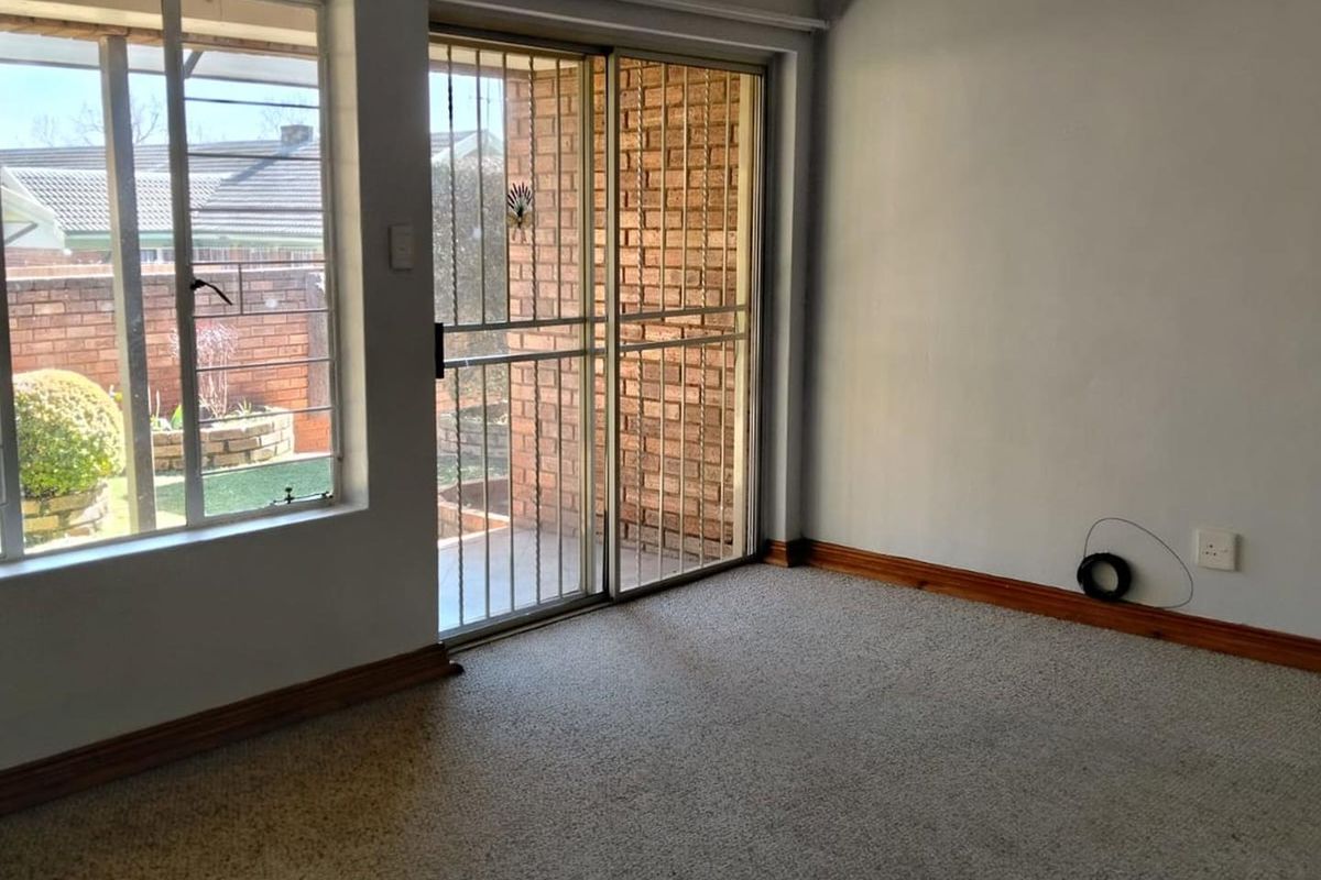 An empty living room featuring carpet flooring, timber skirting, and a sliding glass door with a security gate leading to the exterior.