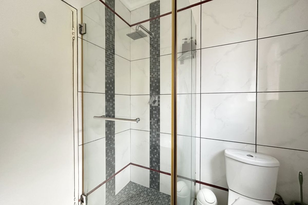 A clean bathroom featuring a glass-enclosed shower with a rain shower head, mosaic tile accents, and a standard toilet.