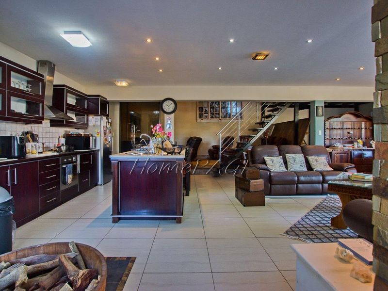 Spacious open-plan living area featuring a modern kitchen with dark cabinetry, a central island, and an integrated staircase leading to the upper level.