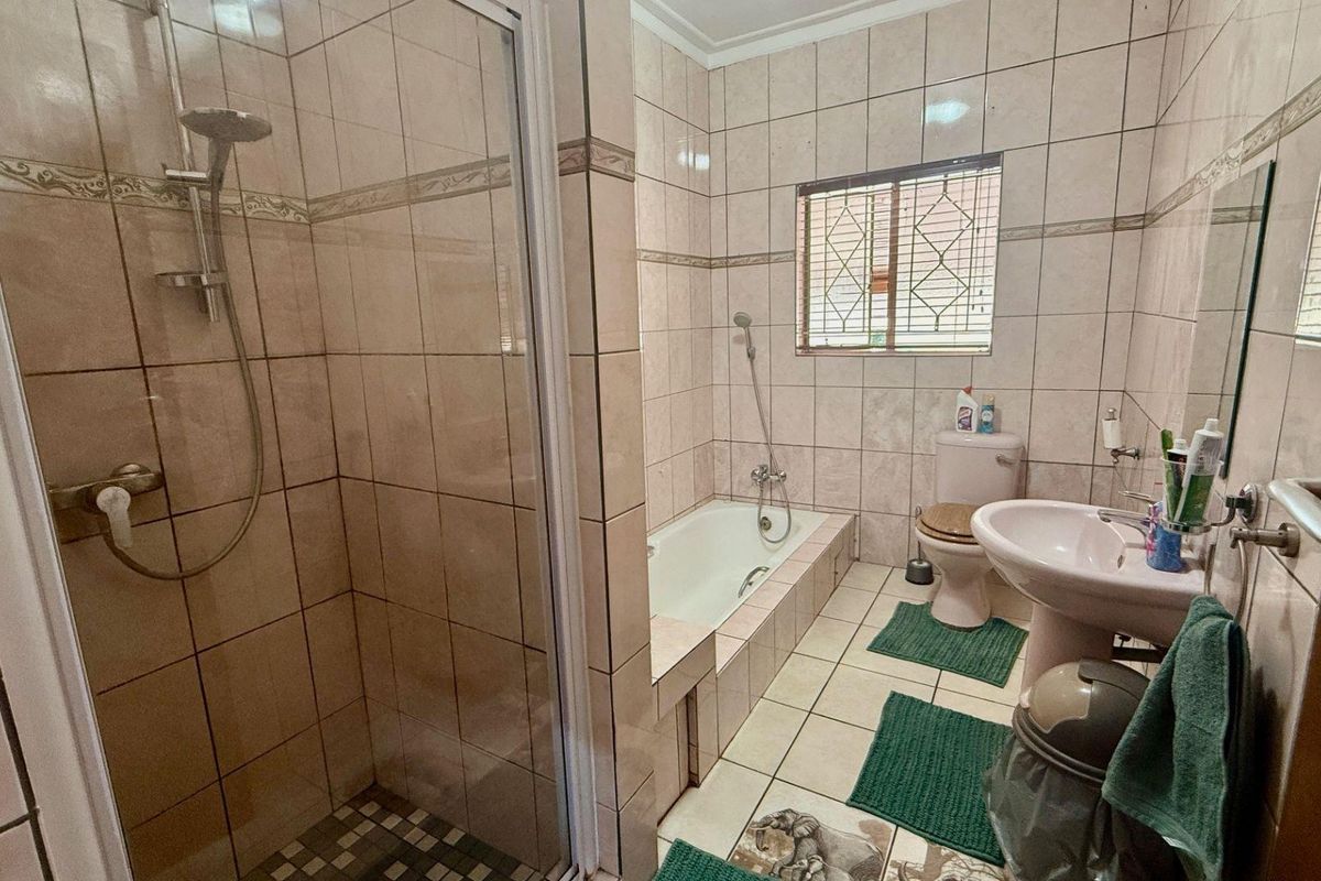 A functional bathroom featuring a separate shower enclosure, a built-in bathtub, a pedestal basin, and a toilet with tiled walls and flooring.