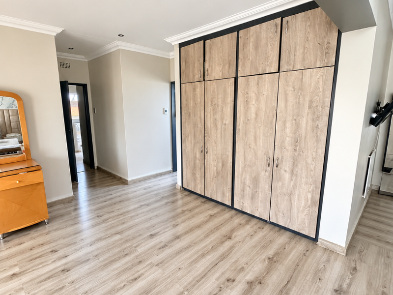 Spacious bedroom featuring modern wood-look laminate flooring, built-in cupboards with a contemporary finish, and recessed ceiling lighting.