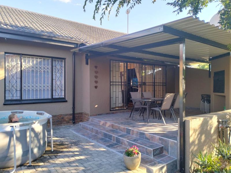 A covered patio area featuring tiled flooring, a built-in braai, and direct access to the home through security gates.