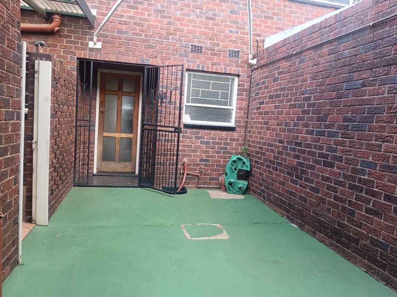 A private rear courtyard featuring brick walls, a security gate, and a painted concrete patio area.