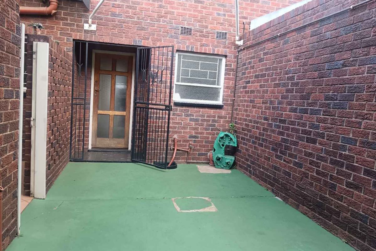 A private rear courtyard featuring brick walls, a security gate, and a painted concrete patio area.