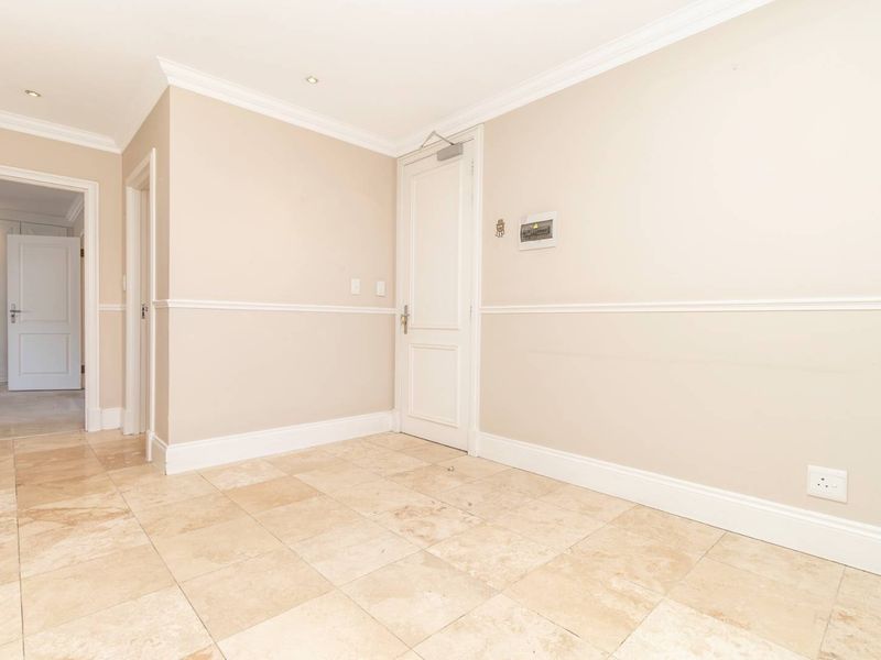 A bright, neutral hallway featuring travertine floor tiles, crown molding, and a dado rail, providing a clean and well-maintained transition space.