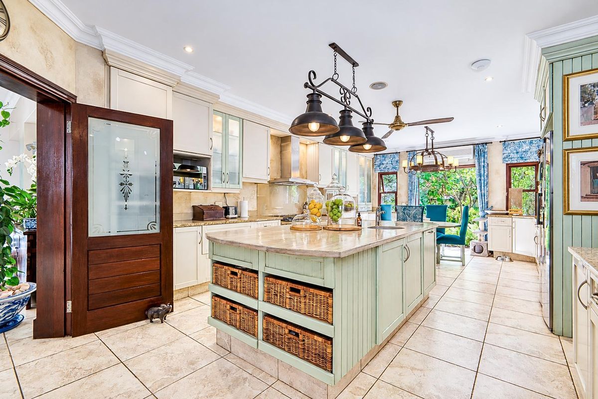 Spacious kitchen featuring a central island with stone countertops, custom cabinetry, integrated appliances, and tiled flooring, opening to a bright dining area.