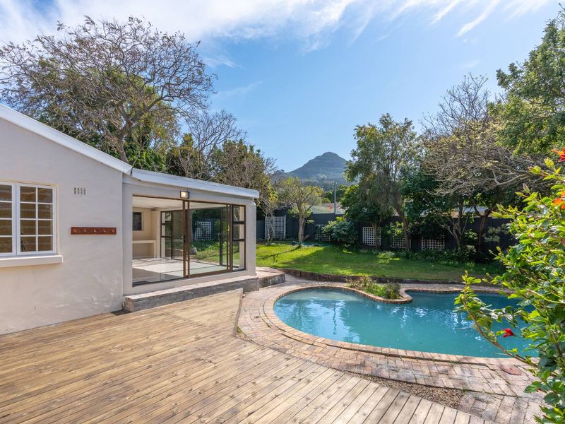 A well-maintained rear garden featuring a swimming pool, timber decking, and a covered patio area with mountain views.