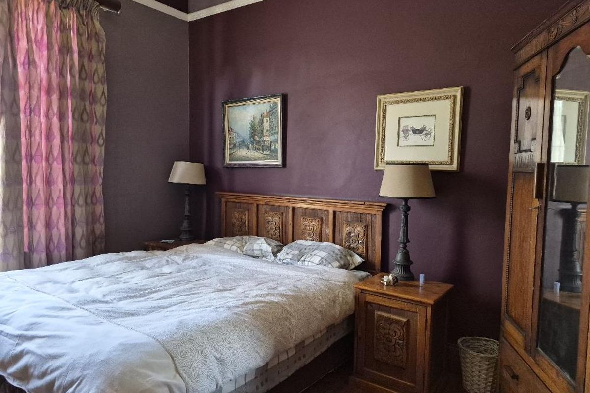 A bedroom featuring dark purple walls, hardwood flooring, and a classic picture rail, providing a cozy and traditional atmosphere.