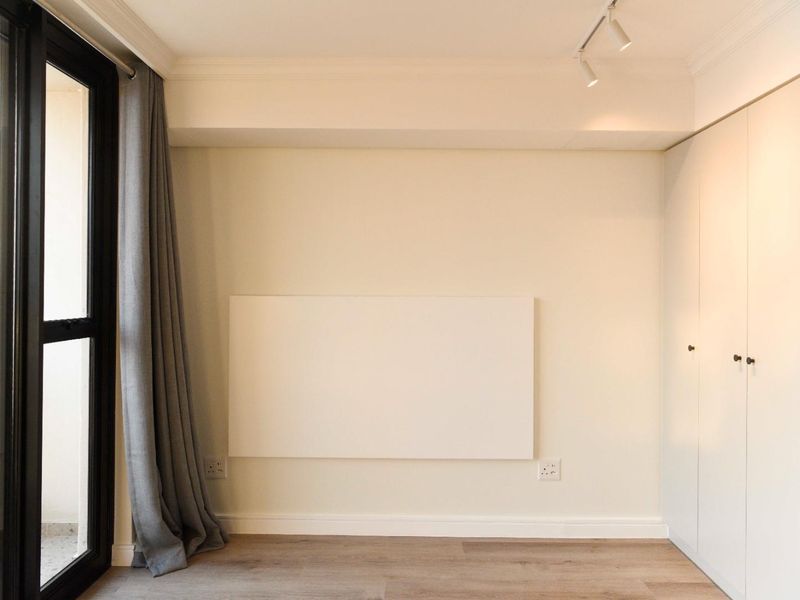 A clean, modern bedroom featuring light laminate flooring, built-in wardrobes, track lighting, and a sliding glass door leading to an outdoor area.