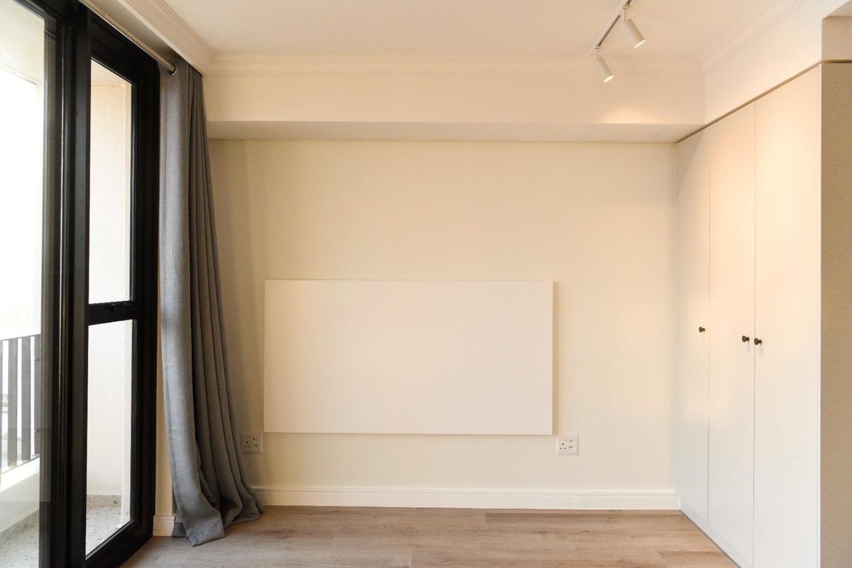 A clean, modern bedroom featuring light laminate flooring, built-in wardrobes, track lighting, and a sliding glass door leading to an outdoor area.