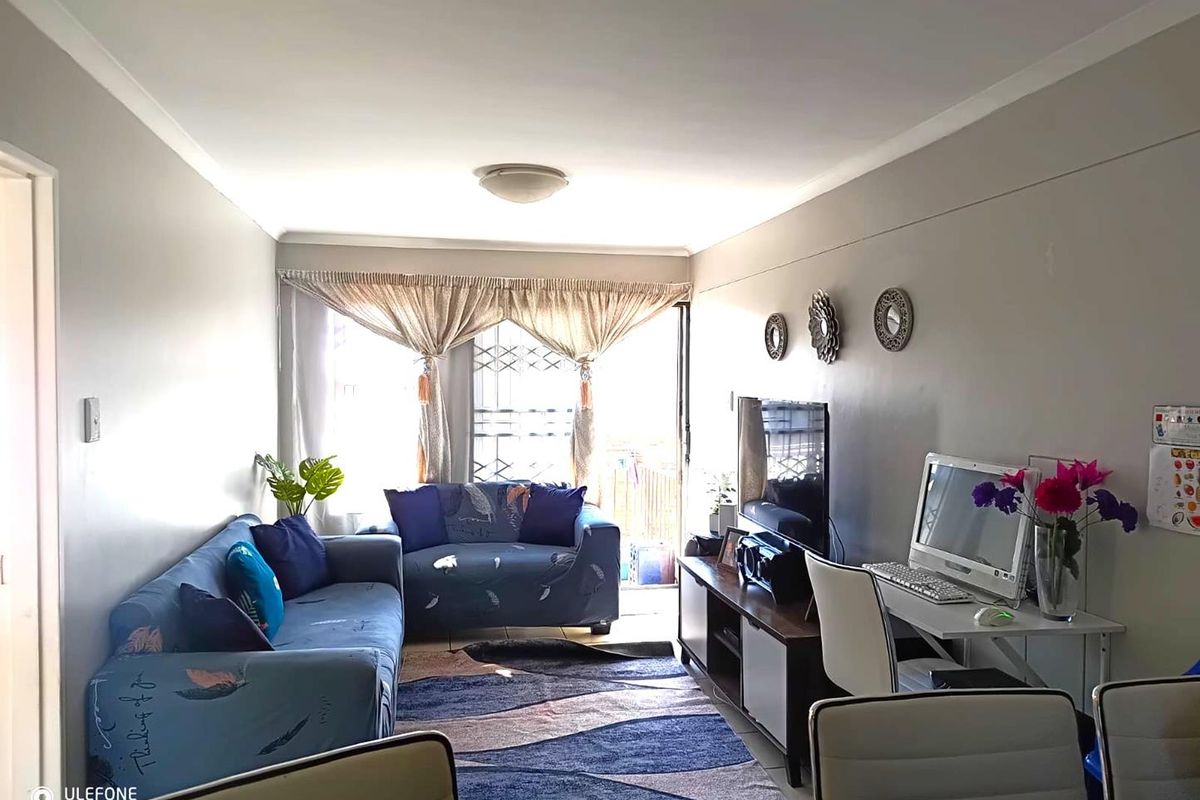 A functional living room featuring tiled flooring, cove cornicing, and a security gate leading to an outdoor area.