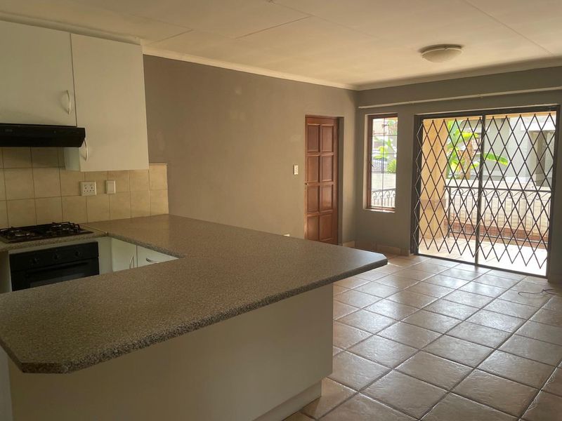 Open-plan kitchen and living area featuring tiled flooring, built-in cabinetry with gas hob, and sliding door access to an outdoor space.