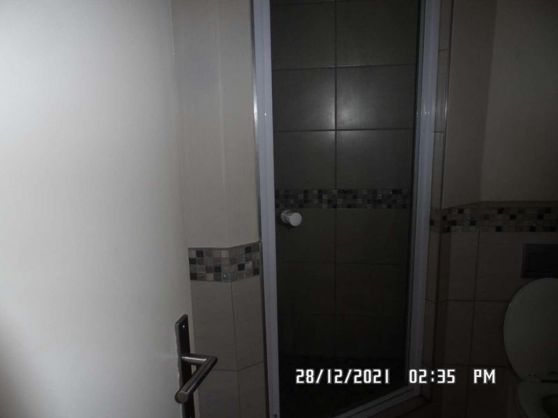 A functional bathroom featuring a shower enclosure with tiled walls, a decorative mosaic border, and a standard toilet.