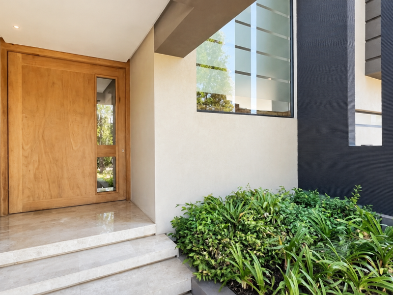 Modern entrance featuring a solid timber front door, marble tiled steps, and a striking dark textured feature wall with large glass window.