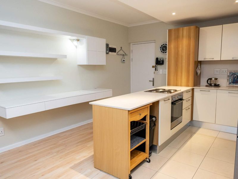 Modern open-plan kitchen featuring sleek cabinetry, integrated appliances, floating shelving, and a functional layout with a mix of tiled and laminate flooring.