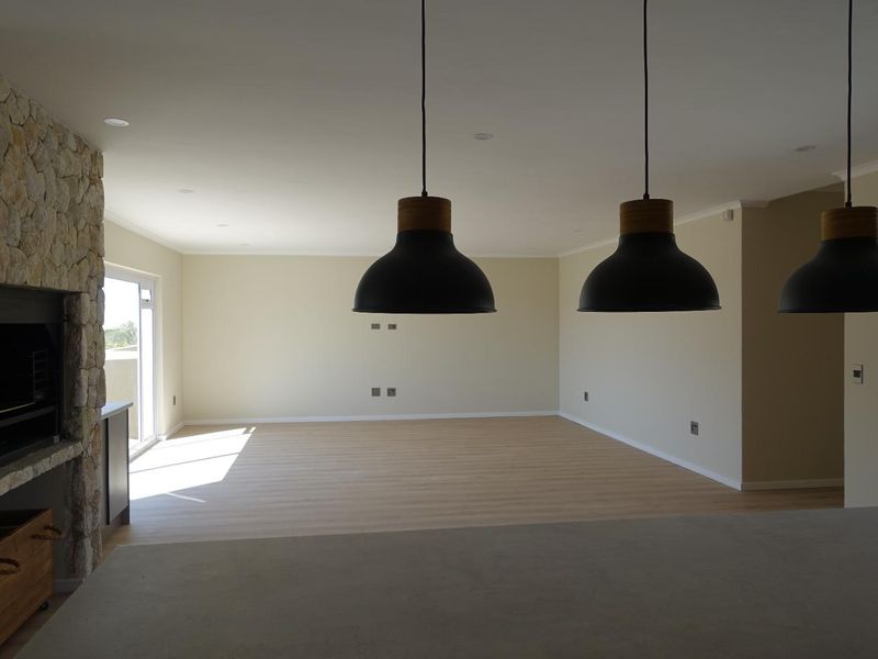 Spacious open-plan living area featuring a stone-clad fireplace, modern pendant lighting, and light laminate flooring with access to an outdoor space.