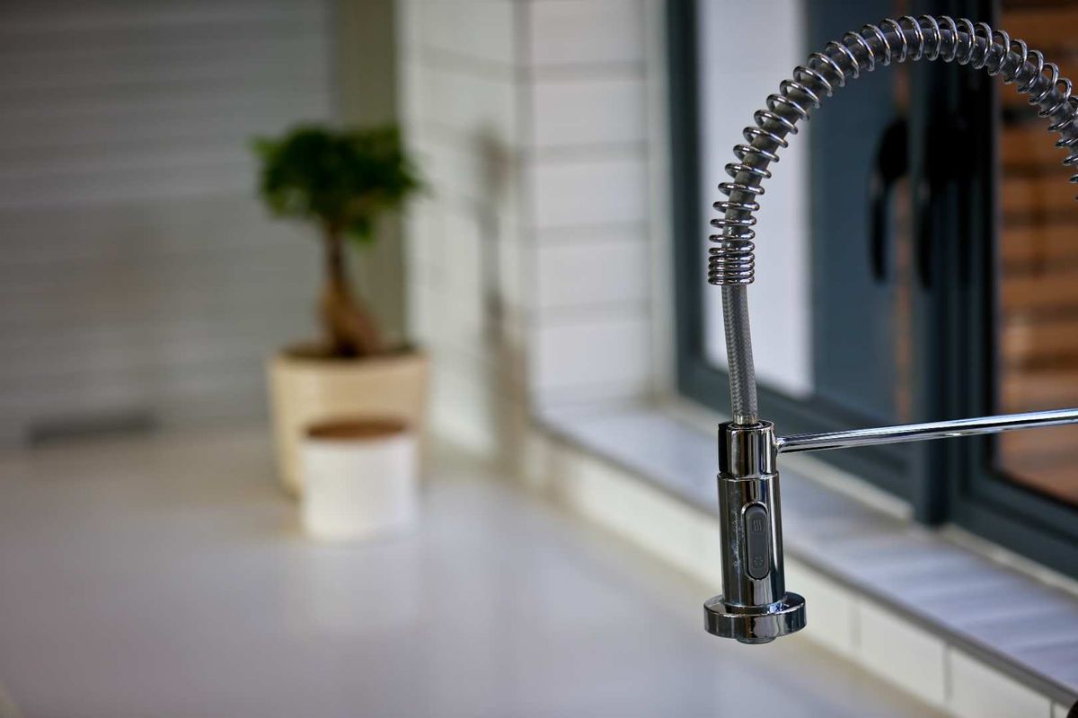 Close-up view of a modern chrome pull-down kitchen faucet with a spring-loaded neck, set against a tiled backsplash and window frame.