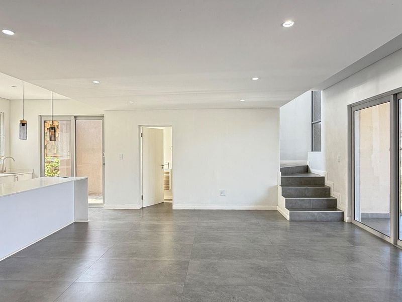 Spacious open-plan living and kitchen area featuring modern tiled flooring, recessed lighting, a central island, and direct access to outdoor spaces via sliding doors.