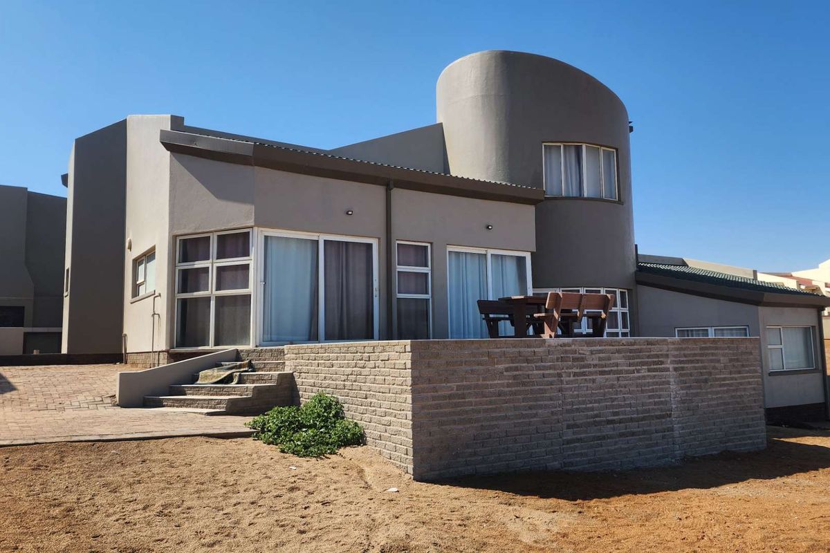 Rear view of a modern house featuring a curved architectural design, sliding glass doors, and a raised brick patio area.