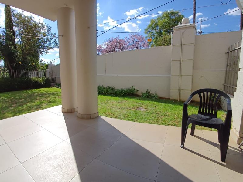 A covered patio area featuring tiled flooring and structural columns, overlooking a private garden space enclosed by a perimeter boundary wall.