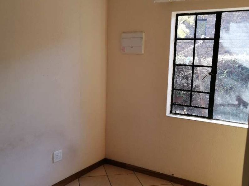 An empty bedroom featuring tiled flooring and a window with security bars, requiring minor cosmetic updates to the wall finishes.