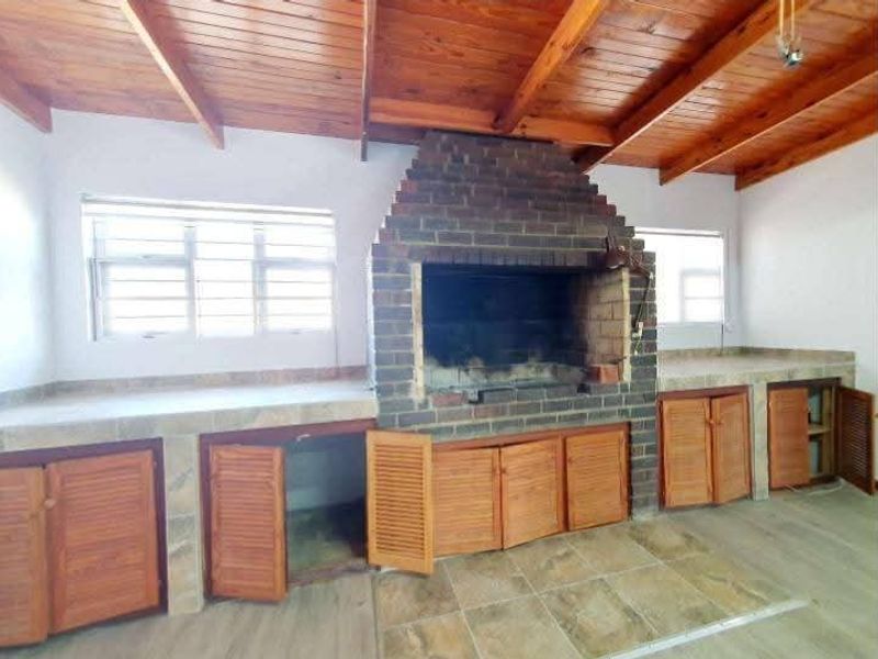 An indoor entertainment area featuring a large built-in brick braai, timber beam ceiling, and tiled preparation counters with wooden cabinetry.
