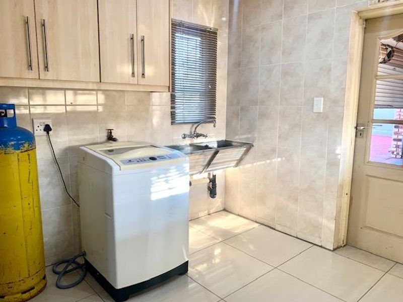 A functional laundry room featuring tiled walls and flooring, built-in cabinetry, and a stainless steel double sink with plumbing connections.